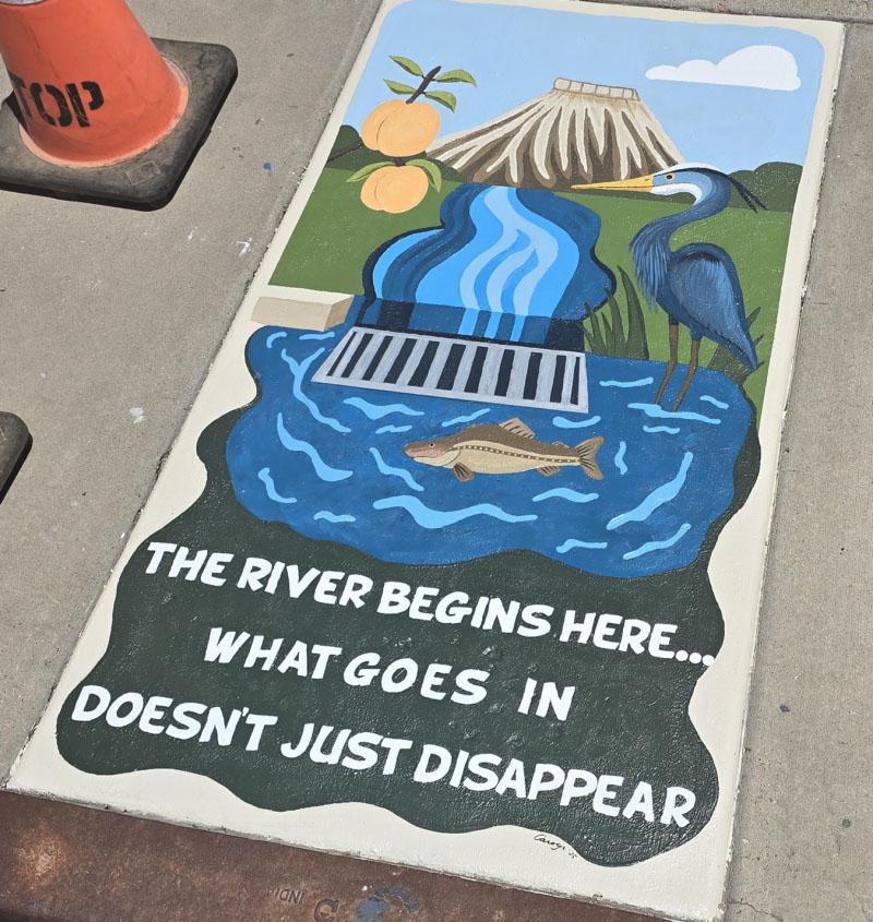Painting on a sidewalk representing Mount Garfield and the water run-off to a drain with text that says The River Begins Here... What Goes in Doesn't Just Disappear. 