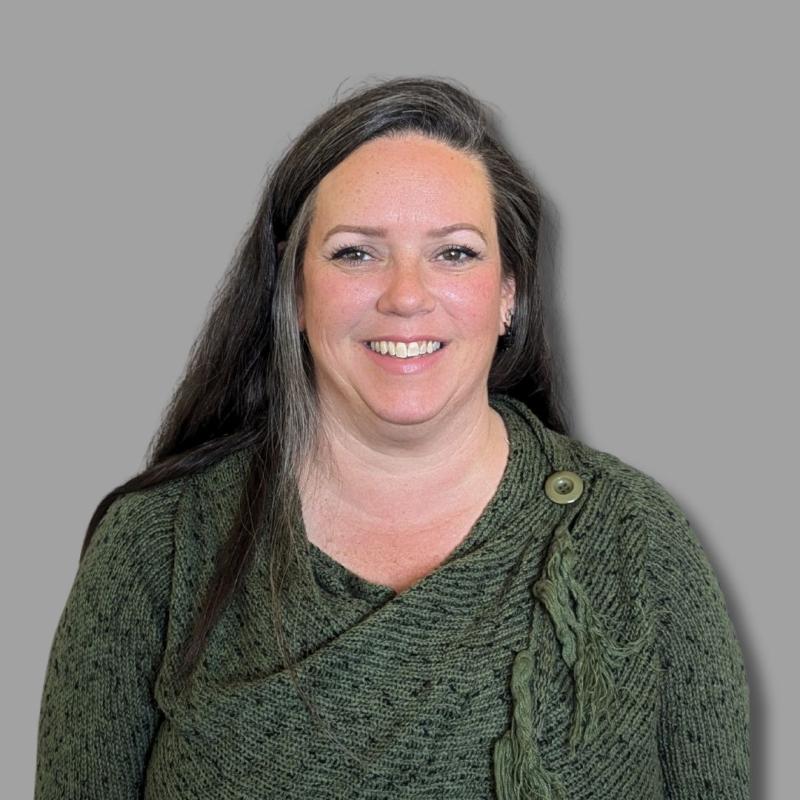 Woman with long black hair smiling in professional photograph, wearing a green sweater.