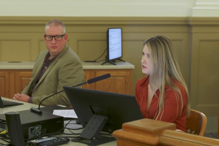Two people sitting at a desk with a microphone. 