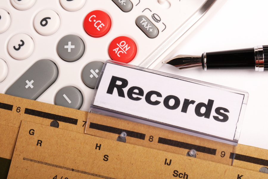 A close-up image of financial and records-related materials, including a calculator, fountain pen, file folder and a label reading “Records.”