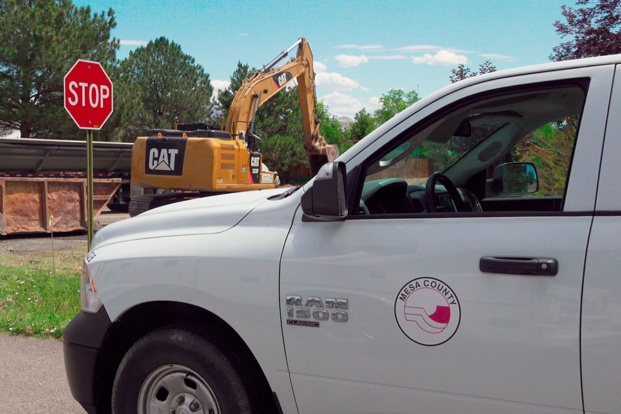 A Mesa County vehicle is parked near active construction equipment as work continues on the 22 1/2 Road and Greenbelt Drive Sidewalk and Drainage Improvements Project in the Redlands area.