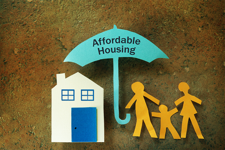 Paper-cut illustration of a house and a family standing beneath a blue umbrella labeled "Affordable Housing," symbolizing housing support and affordability.