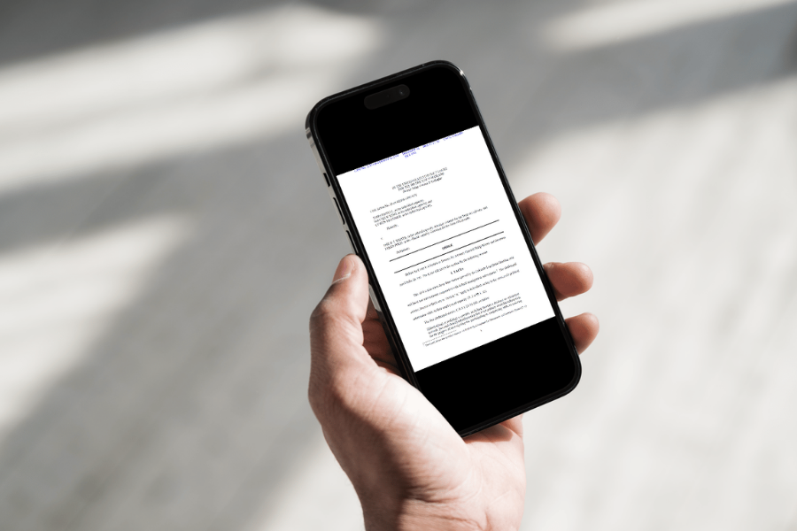 A person holds a smartphone displaying a legal court order or judicial document on the screen against a blurred indoor background. 